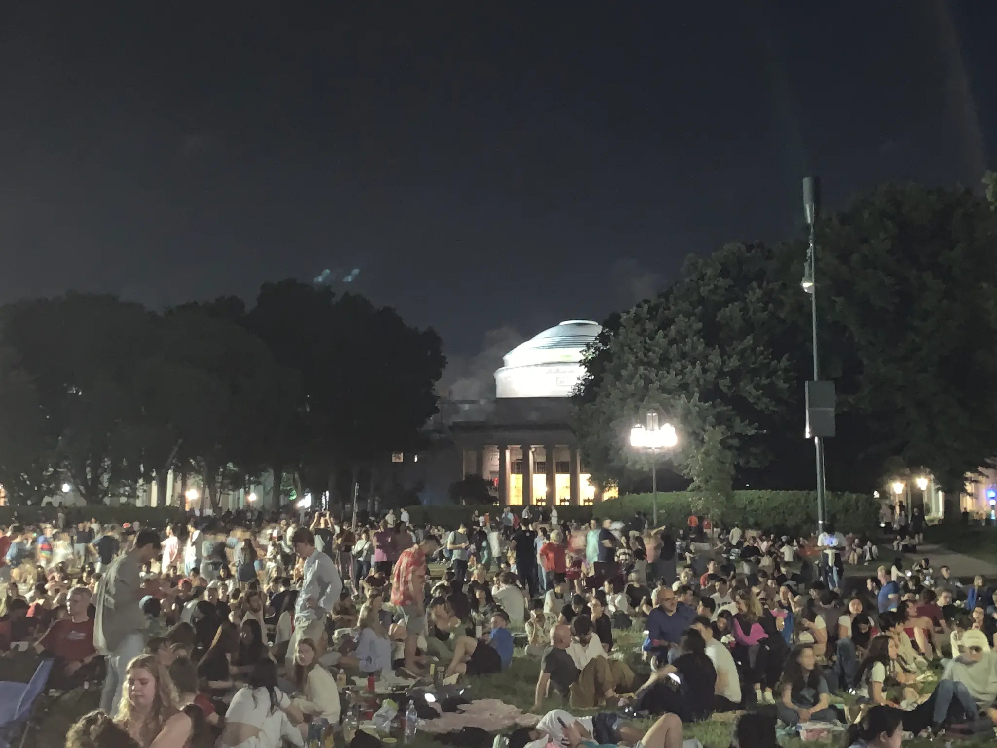 Community gathering on the lawn in front of the MIT Great Dome at night