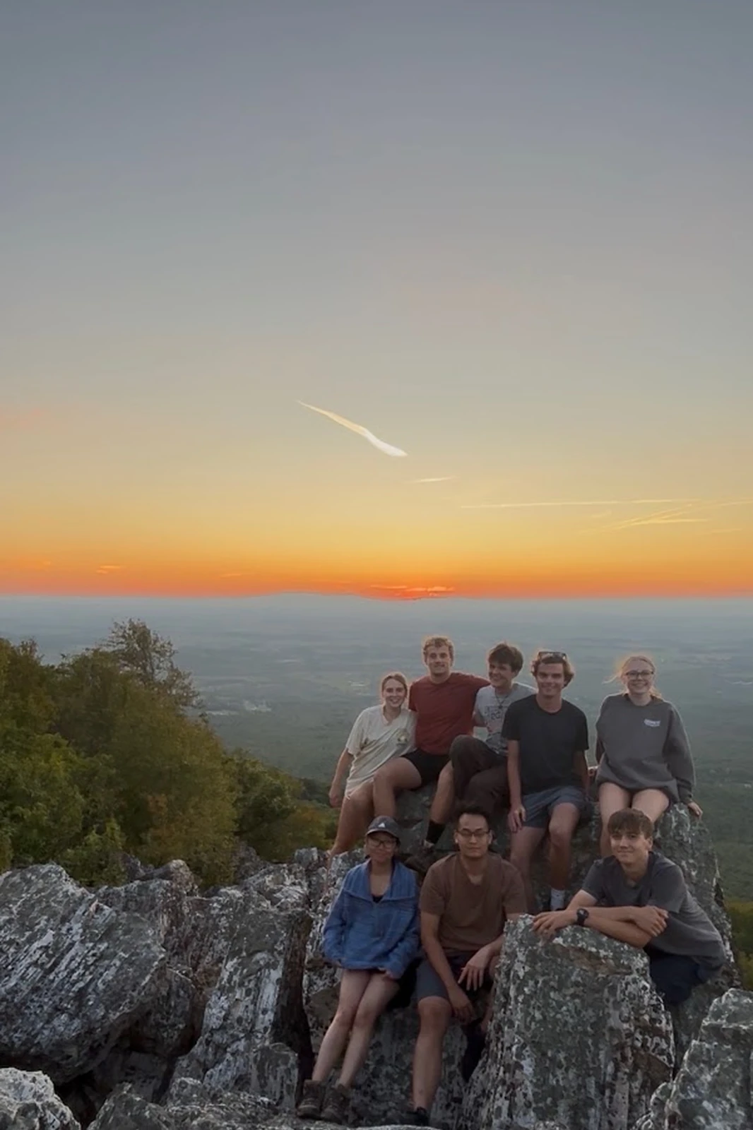 A group of hikers seated on a rocky mountain overlook at sunset