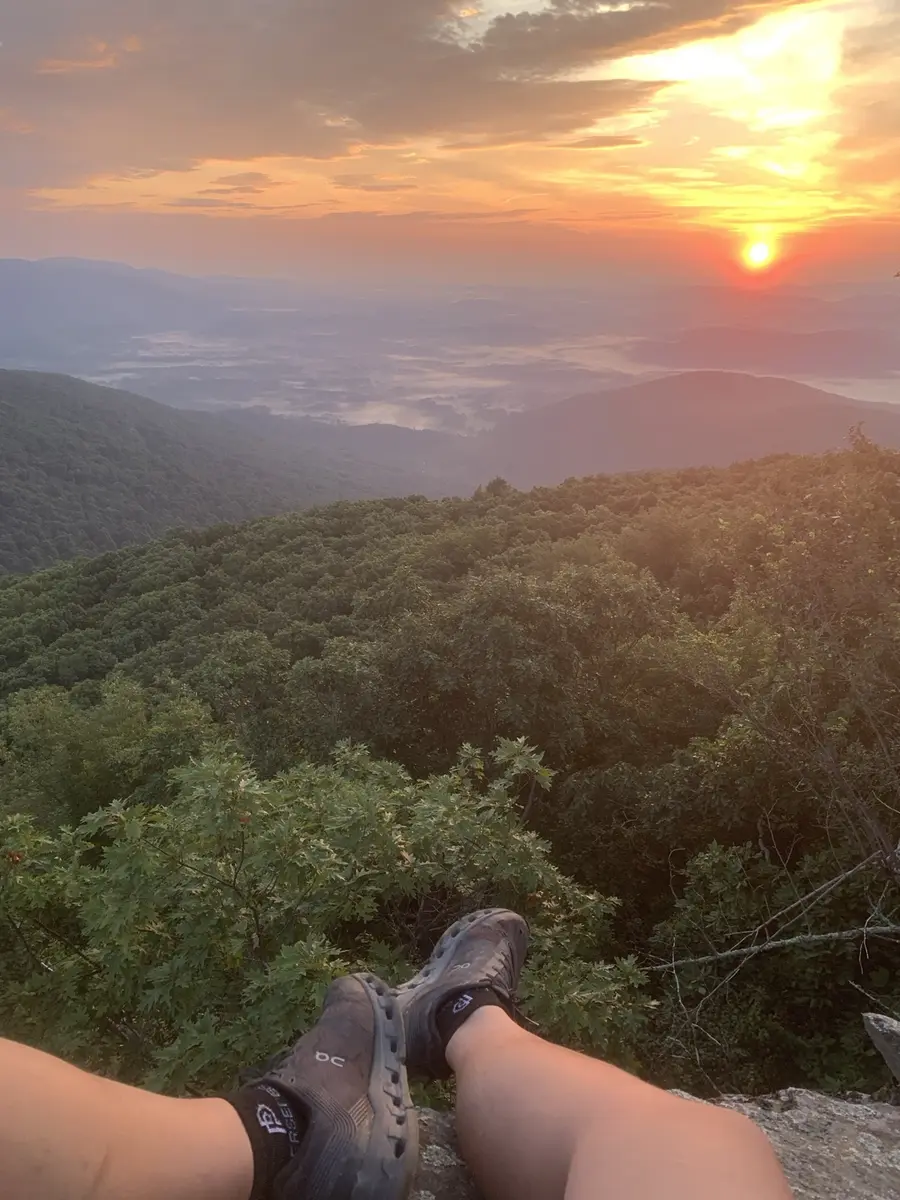 Hiking shoes resting above a forested mountain valley at sunset