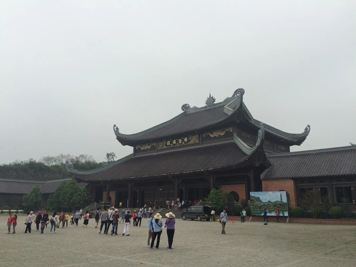 Visitors in a traditional temple courtyard with wooded hills behind