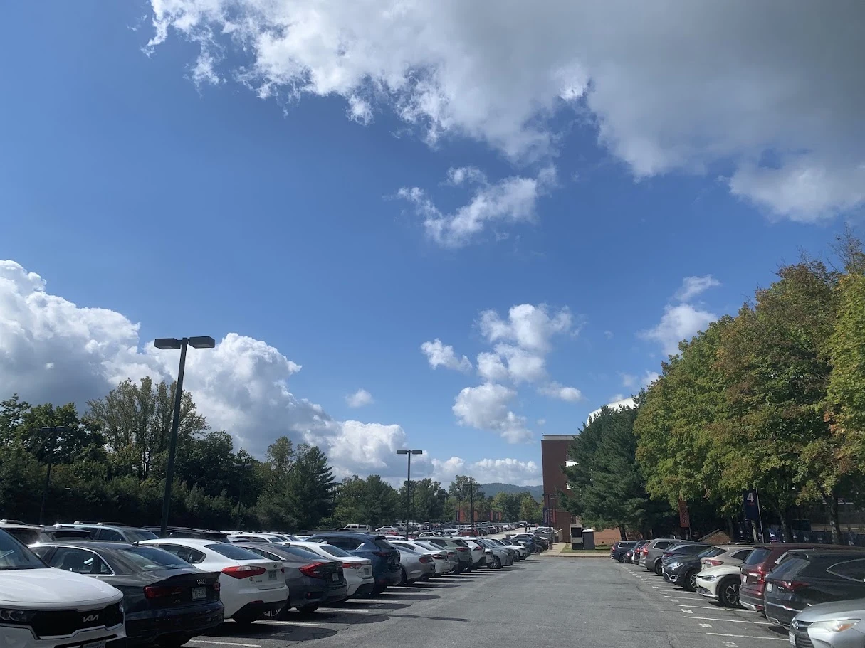 Blue sky and white clouds above a tree-lined parking area