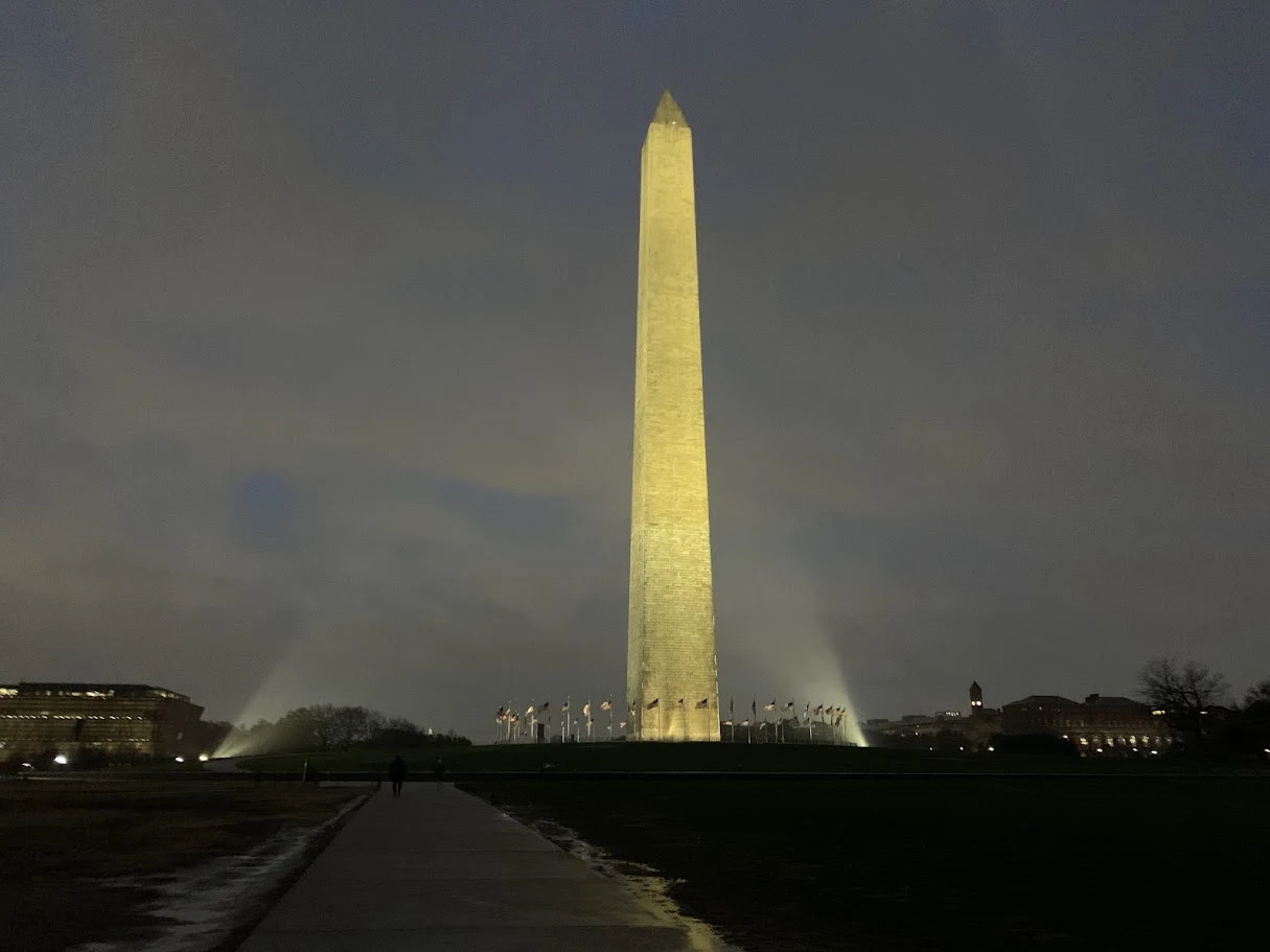 Washington Monument illuminated at night beneath a cloudy sky